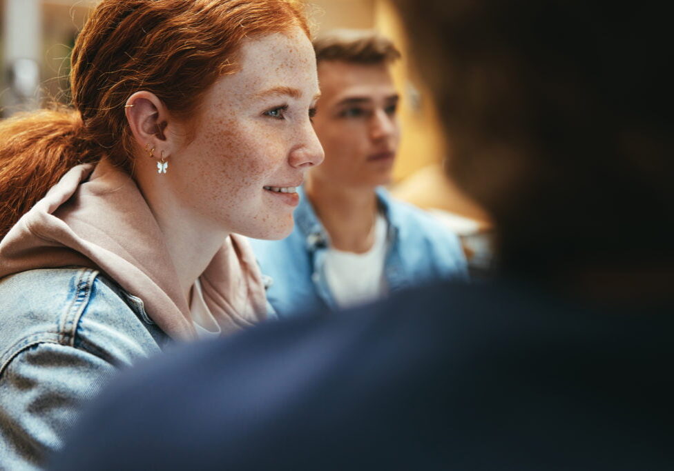 Jente smiler under prosjektdiskusjon i skolebibliotek. Munter jente i gruppearbeid.